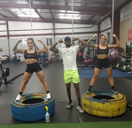 a breaking barriers rowing and fitness trainer flexes his muscles with two female clients