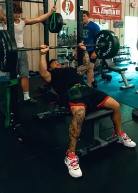one man bench presses while another keeps watch