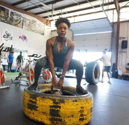 a woman holds a bell weight while squatting on a large tire