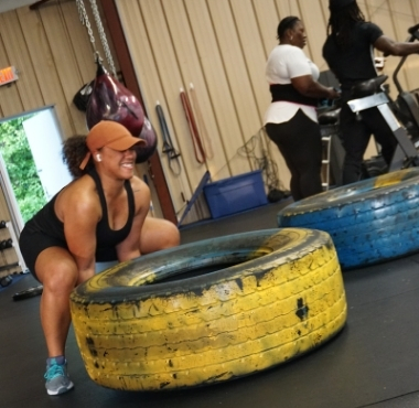 a fit black woman lifts a giant yellow tire during a workout